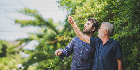 Handsome senior father with young son standing in backyard talking and laughing while looking and...