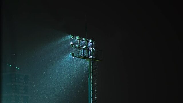 Rack focus of stadium lights in front of a dark blue sky. Light Stadium at night, baseball and hockey. There is a rain or snow. military security lighting towers, patrol in prison