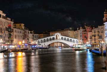 Beautiful view of Grand Canal and Rialto Bridge in Venice, Italy at night with beautiful stars and Milky way galaxy visible in the sky. Romantic style