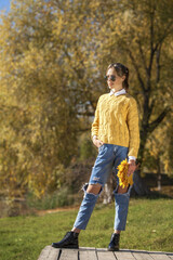 Young girl in a woolen sweater and torn jeans posing in an autumn park