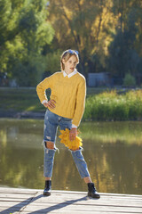 Young girl in a woolen sweater and torn jeans posing in an autumn park