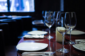 table setting in empty restaurant with clean wineglasses and white candle on wooden table