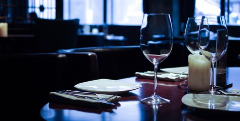 table setting in empty restaurant with clean wineglasses and white candle on wooden table