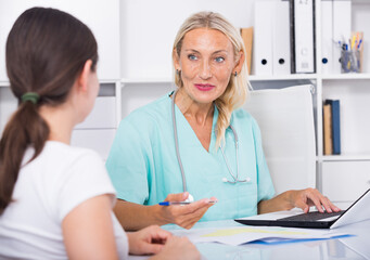 Mature woman physician in blue lab coat consulting female in medical office