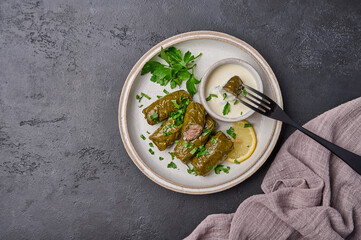 Top view dolma with parsley and lemon in light plate with with sour cream, on black fork pricked piece of dolma over the saucepan
