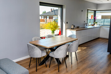 A modern dining room connected to the living room and to the kitchen, there are large windows in the wall, a visible table and chairs.