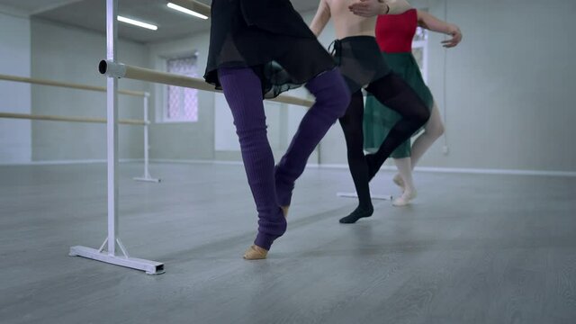 Unrecognizable ballerinas standing at barre rehearsing plie releve movement indoors. Three graceful agile Caucasian slim women dancing in studio. Performance rehearsal concept