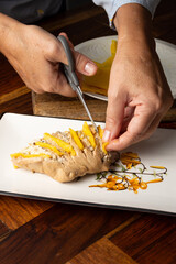 Top view of woman's hands with scissors preparing a turkey breast with handle, on white plate and wooden table, in vertical, with copy space