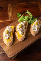 Top view of three toasts with turkey breast pate with cheese, mango and olives, on wooden table and...