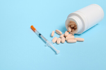 Studio shot of insulin syringe and pharmaceutical pills scattered from a white medicament container on blue background with copy space for medical ad for World Diabetes Awareness Day 14 November.