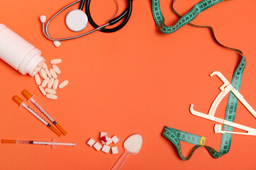Flat lay of white refined sugar with blood drop, caliper, measuring tape, scattered pills, stethoscope and insulin syringes with copy space at orange background center. World Diabetes Awareness Day.