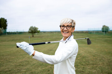 Portrait of senior female golfer in retirement holding golf club at golf course and smiling.