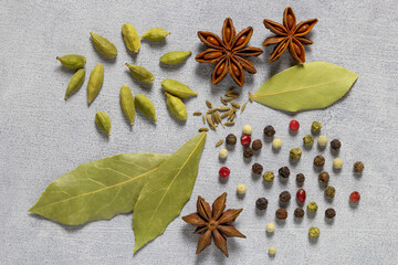 Cardomon, bay leaf, cumin, anise, pepper. Aassorted colorful spices on grey concret background, flat lay, top view.