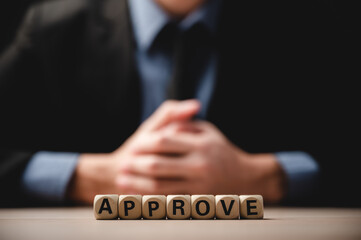 Closeup of wooden cubes with letters and word approve on table with unrecognized man in formal clothing of suit and tie sitting with hands placed on desk during a job interview