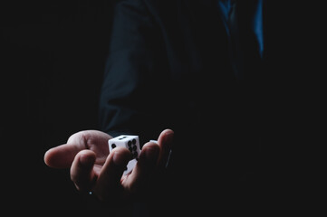 Closeup of hands of a young male entrepreneur and businessman in formal suit clothing rolling dice in a dark pitched background