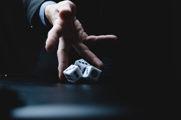 Closeup of hands of a young male entrepreneur and businessman in formal suit clothing rolling dice...