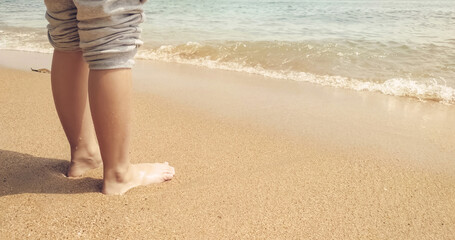 A child's wet feet relaxing on the sand. Kid on vacation. Sea waves on the tropical beach. Warm natural sunlight and clear water.