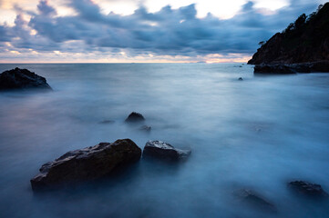 Silent and calm ocean and sea water flowing against mountain and rocks at sunrise and sunset under a cloudy sky