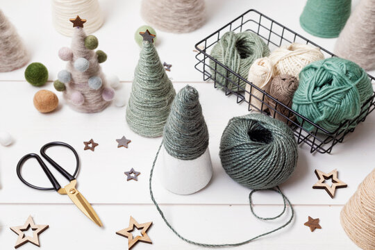 Christmas craft hobby background with handmade yarn cone xmas trees in natural colors. Recomforting, destressing hobby to make christmas decoration. Top view of diy workshop