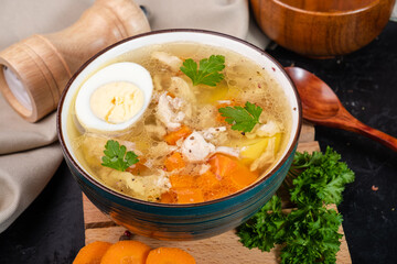Hot chicken soup with meat vegetables and an egg on a black background.