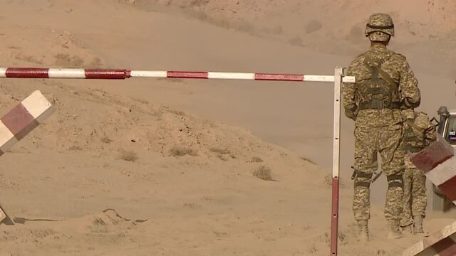 A military patrol stops a car at a checkpoint in a desert war zone. Checking documents, entering the base.