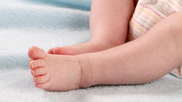 Moving legs, feet and toes of a newborn baby lying on a light blue fleecy blanket, close-up side view.