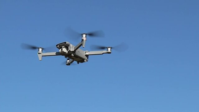 Gray drone flies in the blue clear sky on a summer day, bottom-side view, close-up.