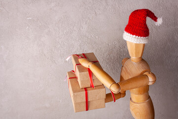 wooden man in a santa hat holds a gift in a red box copy space