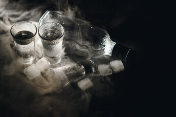 Close-up view of bottle of vodka with glasses standing on ice on black