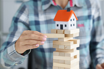 Female hand is listening to wooden blocks on which toy house stands