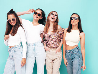 Four young beautiful smiling brunette hipster female in trendy summer clothes. Sexy carefree women posing near blue wall. Positive models having fun. Cheerful and happy in sunglasses