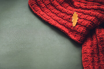Red knitted scarf with an autumn leaf. The concept of warmth and comfort. Space for text, copy space