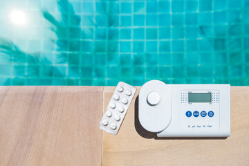 Digital water tester equipment and pool tester tablet on swimming pool edge with space on blue...