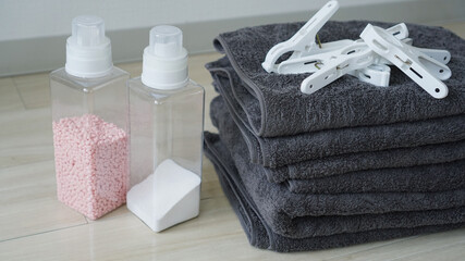床に畳んで重ねられた洗濯物のタオルと洗剤、洗濯バサミのランドリーセット