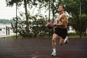 Young shirtless sportsman working out with basketball on playground