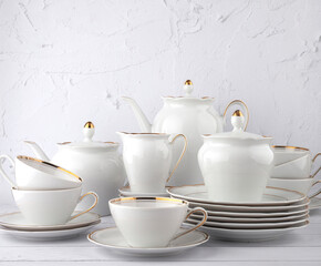White tea set on a white background. Teapot, cream, sugar bowl, cups, saucers, plates on the table. Porcelain dishes. For six persons.
