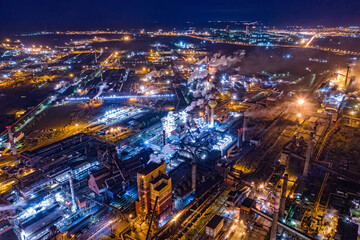 Fototapeta na wymiar Aerial view of steel plant at night with smokestacks and fire blazing out of the pipe. Industrial panoramic landmark with blast furnance of metallurgical production. Concept of environmental pollution