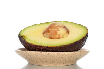 One half of an organic ripe avocado on a ceramic dish, close-up, isolated on white.