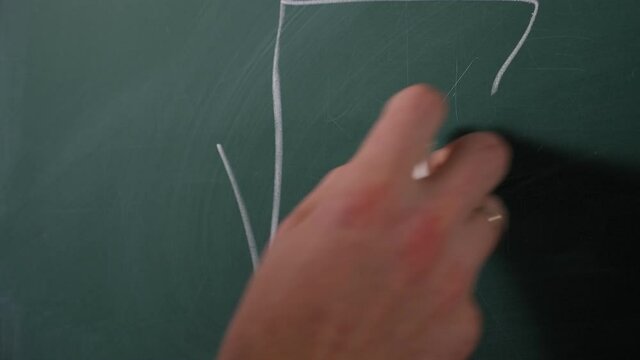 Close-up of a male mathematician writing a formula on a blackboard during a lecture at a university.
