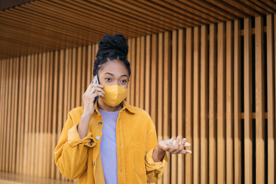Busy Emotional African American Woman Wearing Protective Face Mask Talking On Mobile Phone Walking On The Street. Worried Customer Calling Support Center 