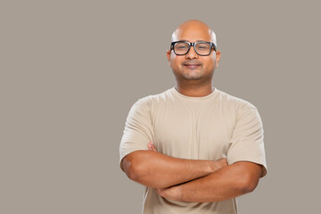 Portrait of a bald man wearing eyeglasses smiling with folded hands against plain background.