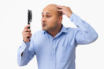 Portrait of a bald man touching his shaved head while looking sadly at comb in his hand.