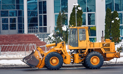 Yellow front loader with scoop for clearing snow. Wheel loader machine ready to removing snow in winter. Municipal service vehicle parked at street. Municipal city service cleans street from snow