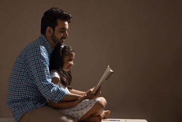 A FATHER AND DAUGHTER HAPPILY SITTING TOGETHER AND READING BOOK