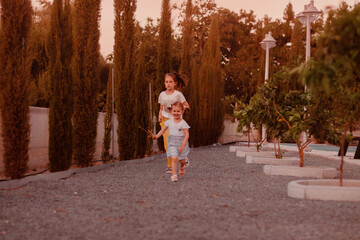 Two little girls playing, running together in park outdoors, big sister nursing younger one.