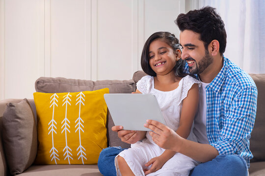 A FATHER AND DAUGHTER LAUGHING TOGETHER WHILE USING DIGITAL TABLET