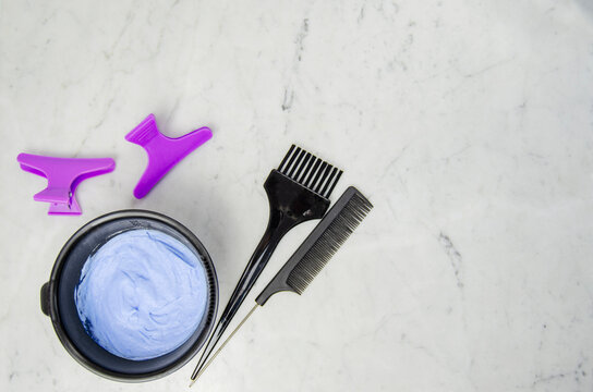 Utencilios decoloraci&oacute;n tinte pelo en polvo azul con peine, pinzas y brocha sobre fondo marmolado