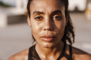 Black sportswoman looking at camera while working out on parking
