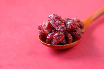 dried cranberries on a wooden spoon on red background 