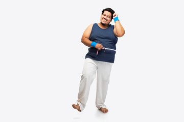 Portrait of a fat man smiling while wrapping measuring tape around his waist against plain background.